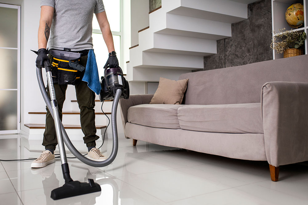 Buildnest staff performing deep cleaning with a vacuum cleaner in a furnished living room after guest checkout — part of Airbnb-style property management and maintenance in Niagara Region.