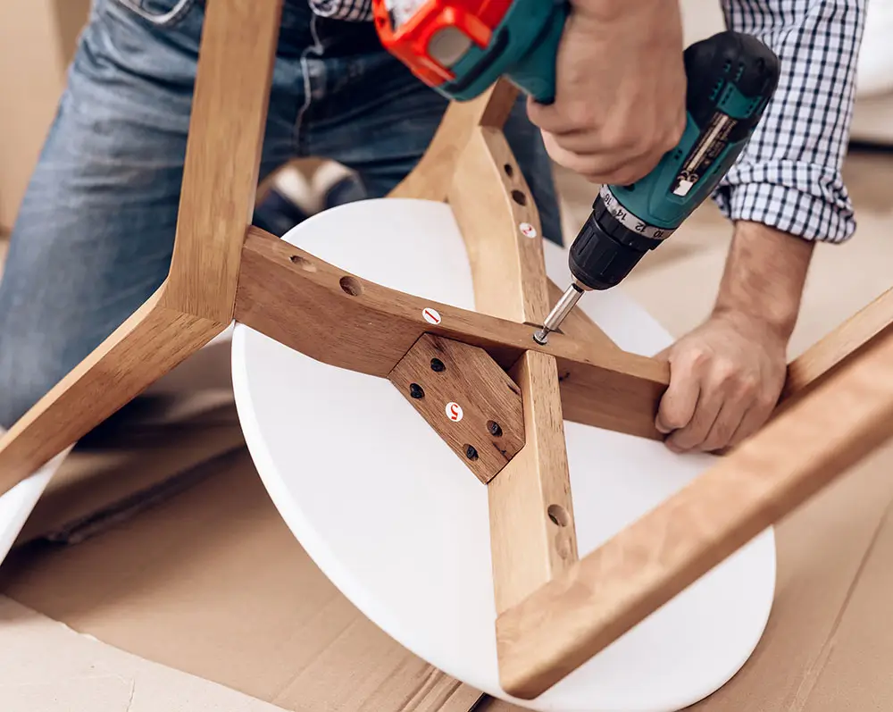 Buildnest handyman assembling a wooden chair using a power drill in Welland, Niagara Region. Expert in furniture assembly, carpentry, and residential handyman services.