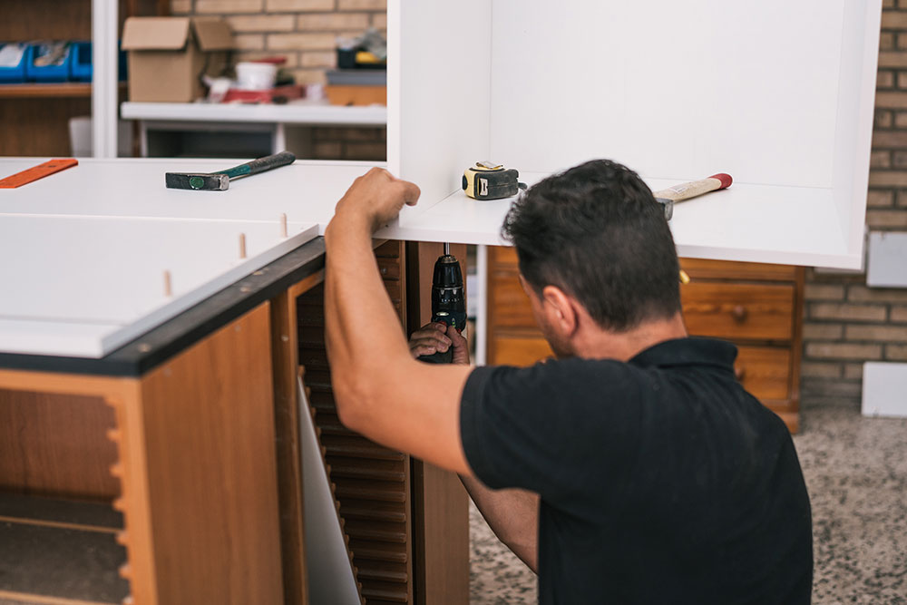 Buildnest handyman installing wooden fixtures in a kitchen using a power drill — delivering expert cabinetry and interior woodwork services in Niagara Region homes.